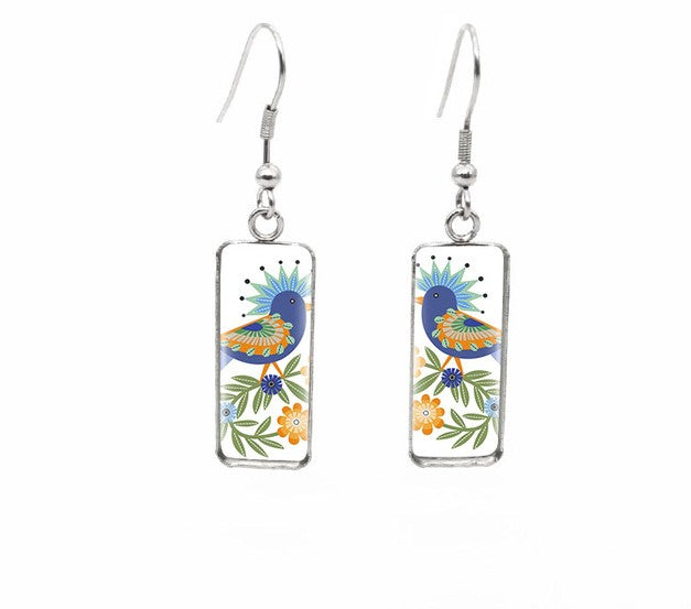 Pair of silver dangle earrings featuring a stylized blue bird with patterned orange wings and a blue feathered crest among green leaves and small orange and blue flowers on a white background