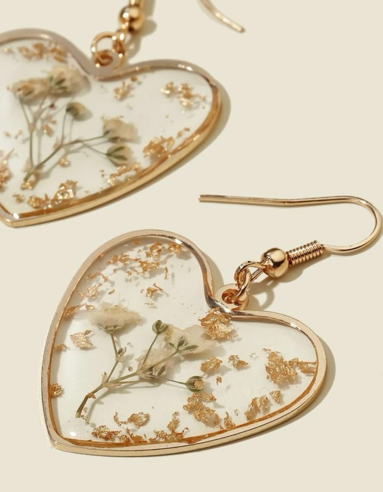 Pair of heart-shaped jewelry dangle earrings featuring clear resin with embedded dried white flowers and scattered gold flakes framed in rose gold