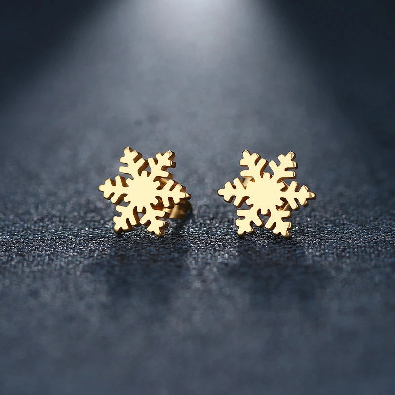 Two golden snowflake stud earrings with intricate six-pointed designs resting on a dark textured surface