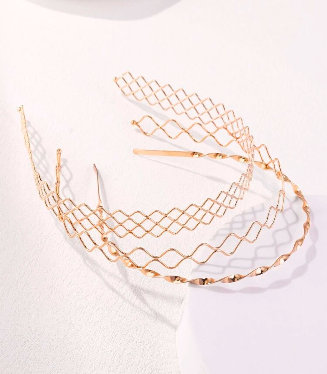 Rose gold metal headbands displaying distinct diamond lattice, wavy undulation, and twisted spiral patterns resting on a clean white surface