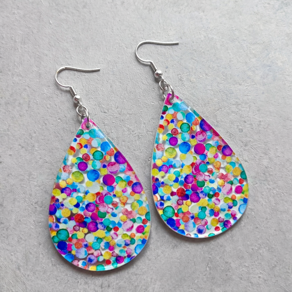Clear resin teardrop earrings featuring a vibrant multicolor confetti dot pattern with silver ear hooks on a grey background