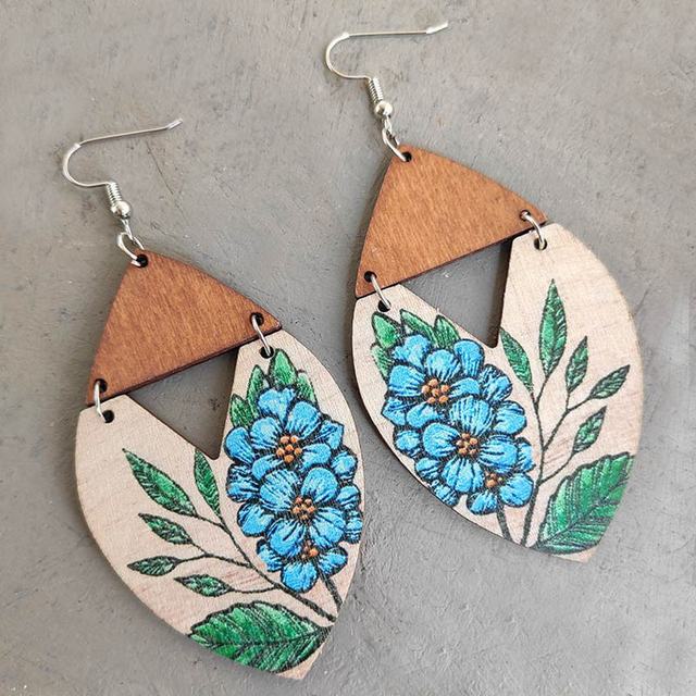 Handcrafted wooden earrings featuring a two-tone design with light brown tops and natural beige marquise-shaped bases intricately hand-painted with clusters of bright blue flowers and green leaves on silver hooks