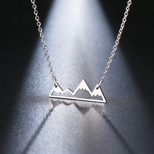 Silver-toned metal necklace featuring a minimalist mountain range silhouette design with a delicate chain reflecting on a dark glossy surface
