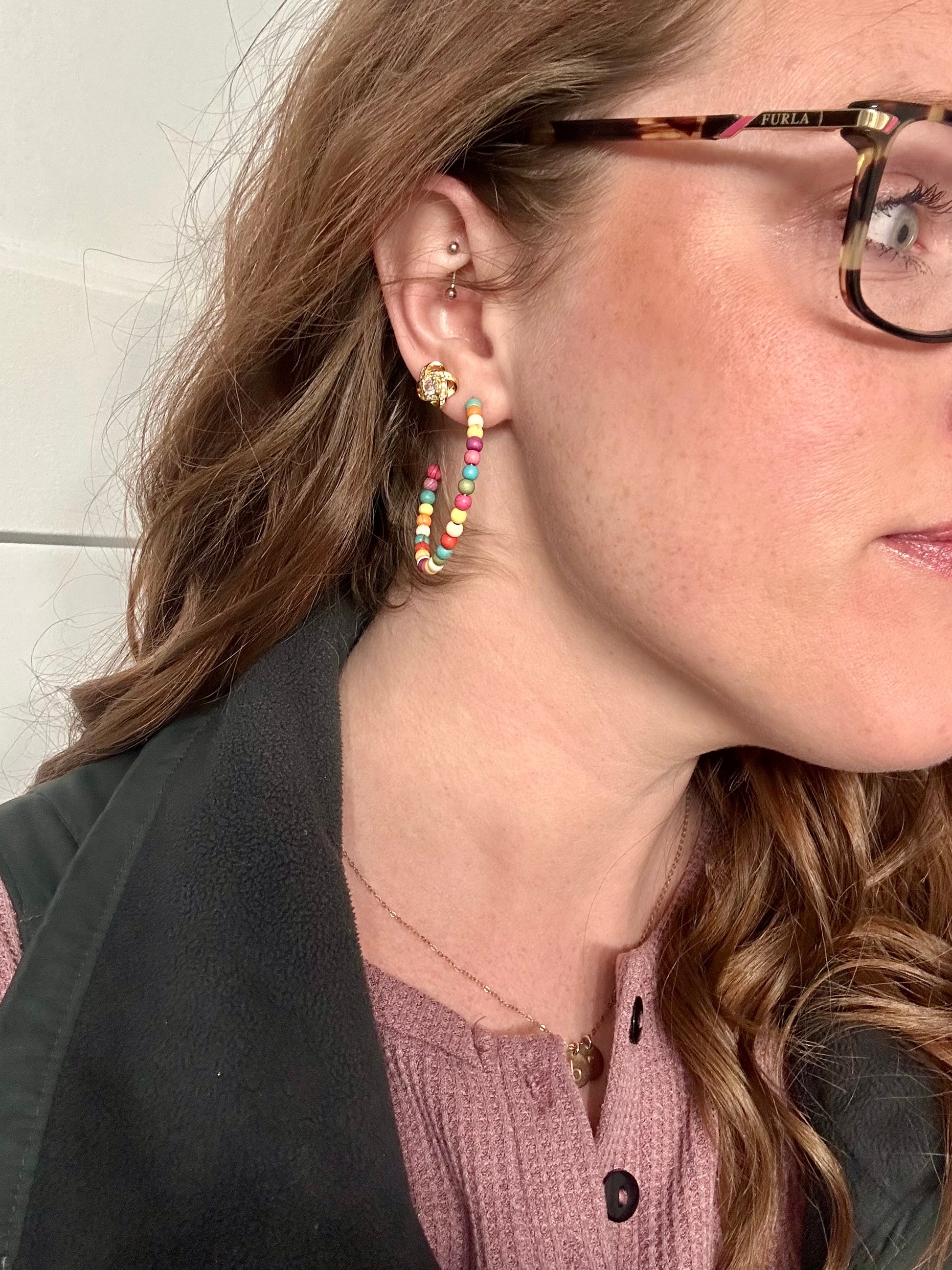 Photo of a woman's profile wearing Furla tortoiseshell glasses, a vibrant beaded hoop earring, and a delicate gold knot stud