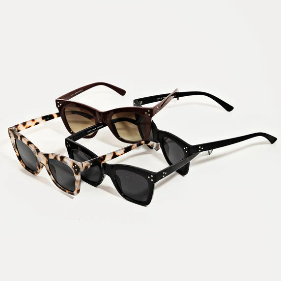 Three pairs of cat-eye sunglasses including white tortoiseshell, dark brown with gradient lenses, and sleek black, all featuring decorative stud details on a plain white background