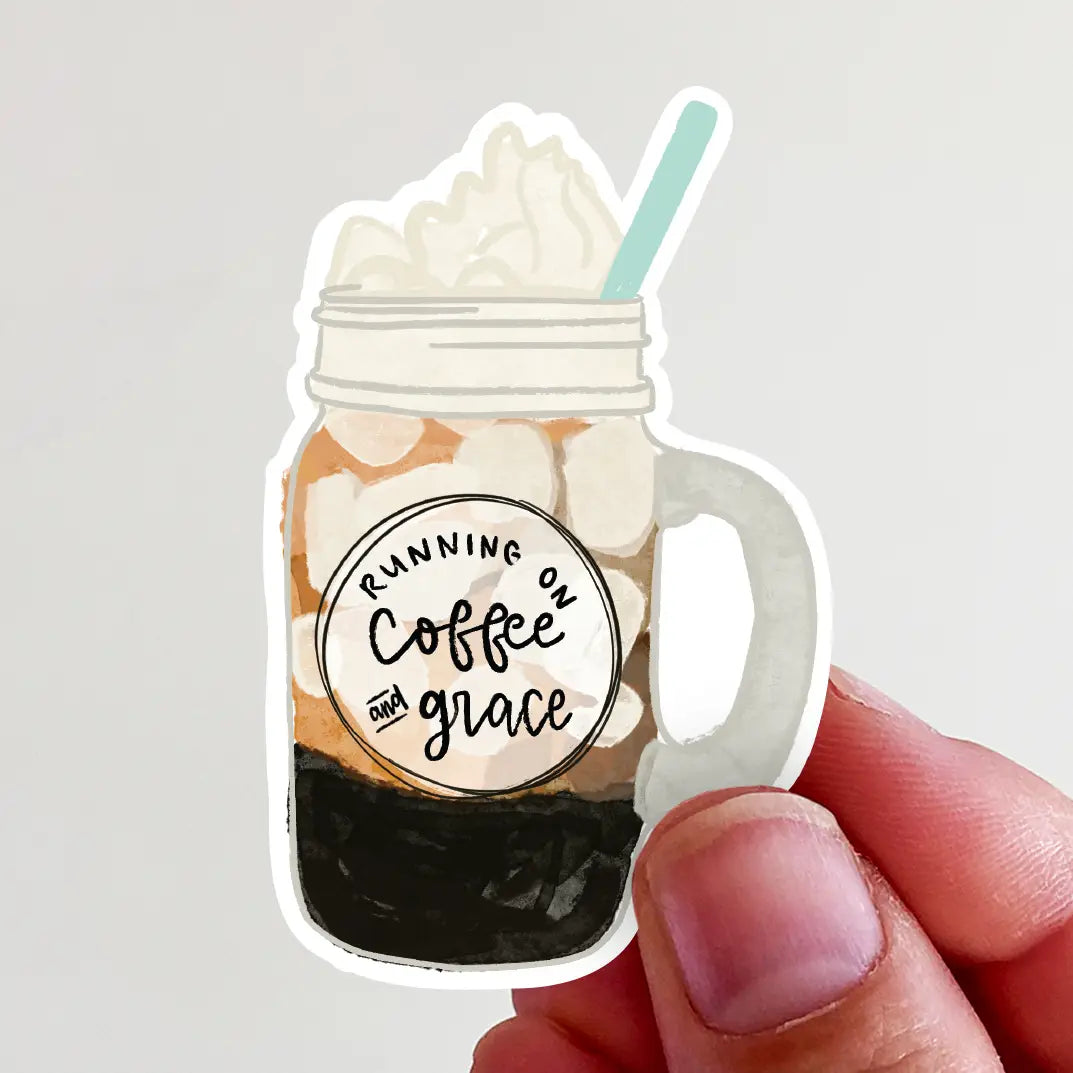 Sticker of a hand holding a mason jar of layered iced coffee topped with whipped cream, a light blue straw, and a circular label with Running on Coffee and Grace text