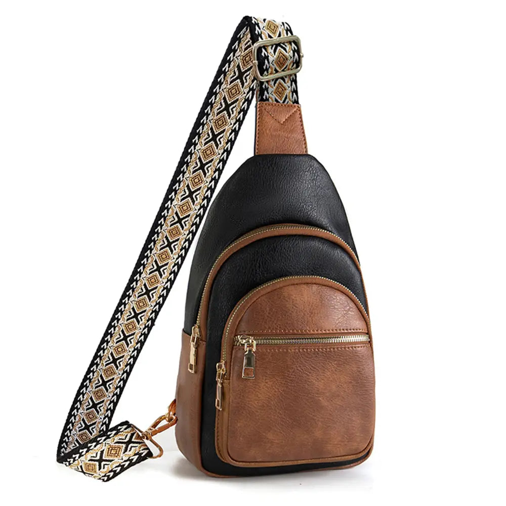 A black and brown faux leather sling bag featuring a distinctive woven geometric patterned strap in gold, black, and white, with two prominent gold zippered front pockets, displayed in a clean studio setting
