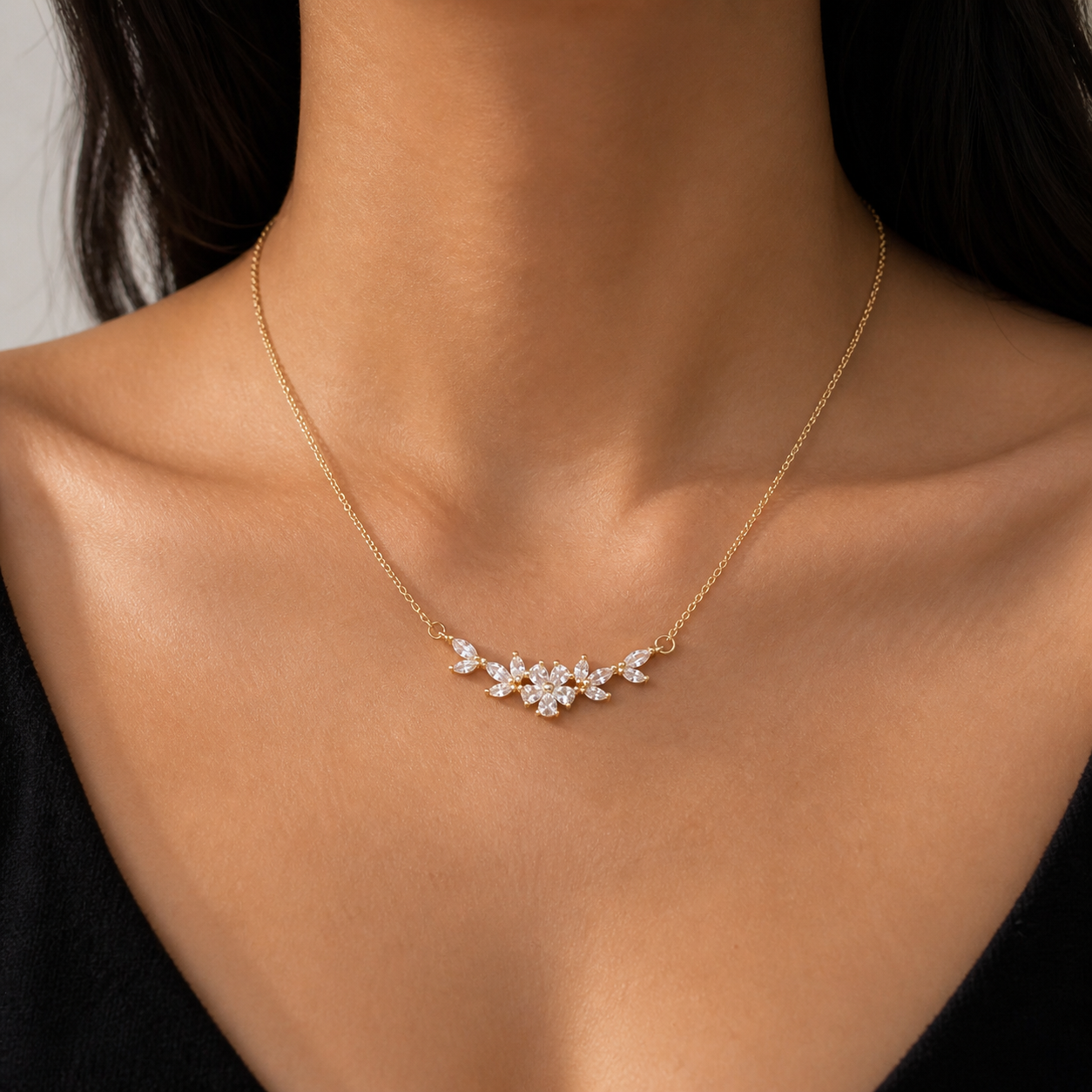 Delicate gold necklace featuring a floral cluster of marquise-cut clear gemstones worn on a woman's décolletage over a black garment