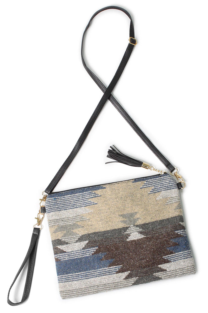 Textile crossbody bag with a Southwestern geometric pattern in earthy beige brown and grey with blue accents featuring a black faux leather adjustable strap gold-tone hardware and a tassel charm
