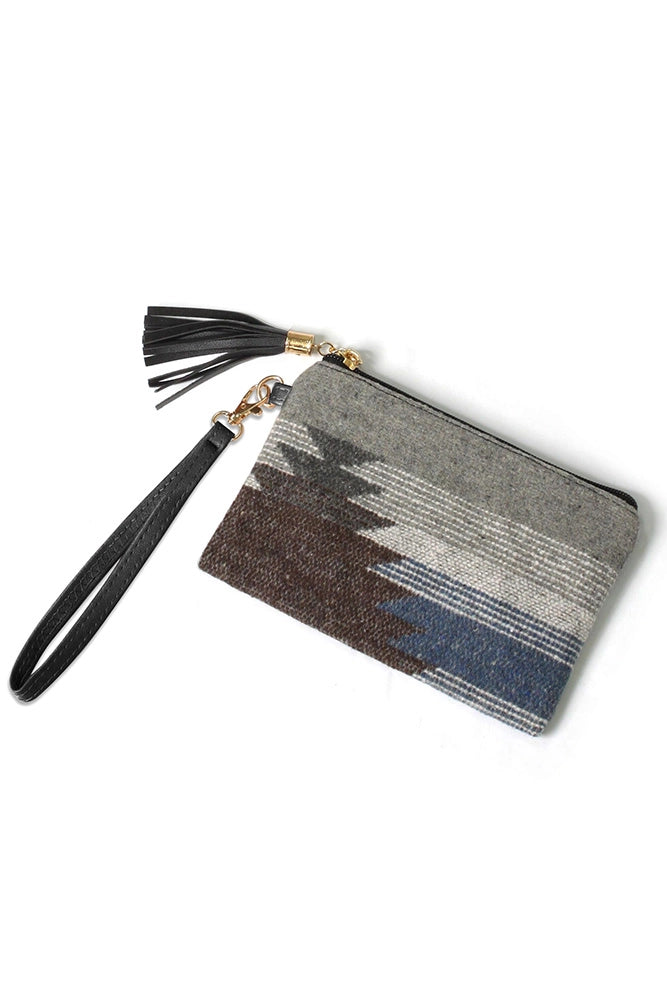 Woven textile wristlet clutch featuring a geometric pattern in shades of grey brown blue and white with a black leather wrist strap and tassel