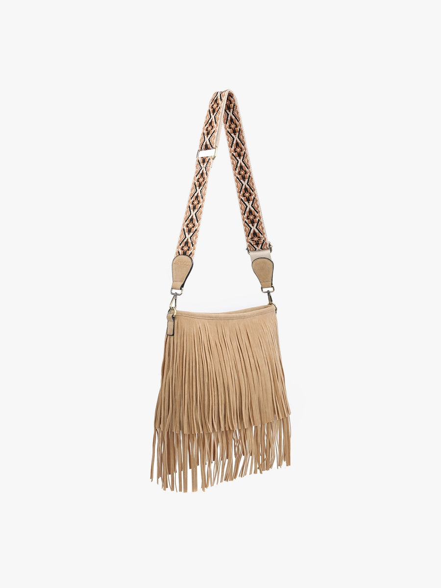 A tan faux suede fringed crossbody bag in a boho style with a detachable black, tan, and cream geometric patterned strap and gold hardware on a white background