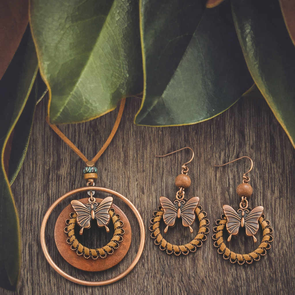 A bohemian copper butterfly jewelry set featuring a pendant on a leather cord with a small blue bead and matching earrings with braided rope accents, displayed on a rustic wooden surface under lush green leaves