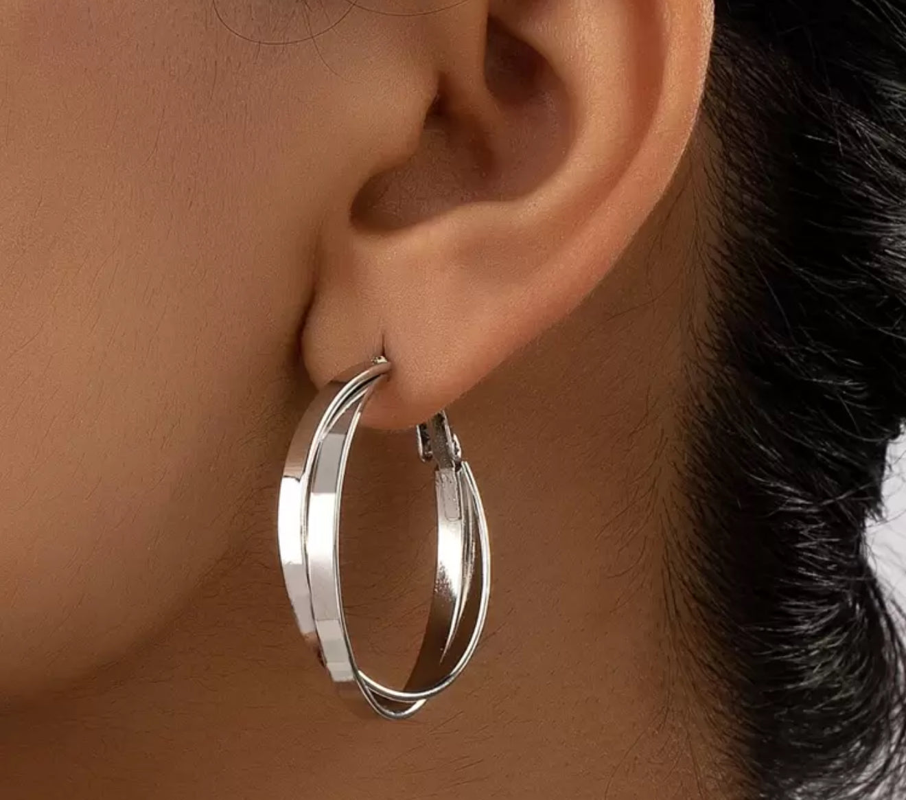 Close-up of a gleaming silver double-banded hoop earring on a person's ear